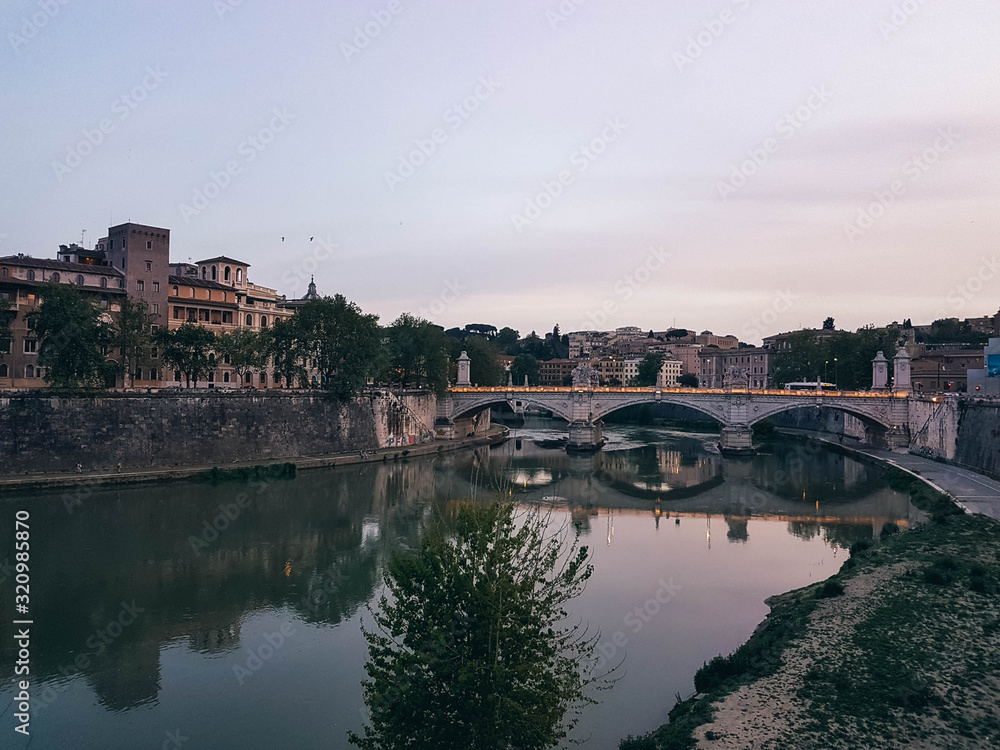 Beautiful river scene in Rome with a bridge and houses at early evening.	