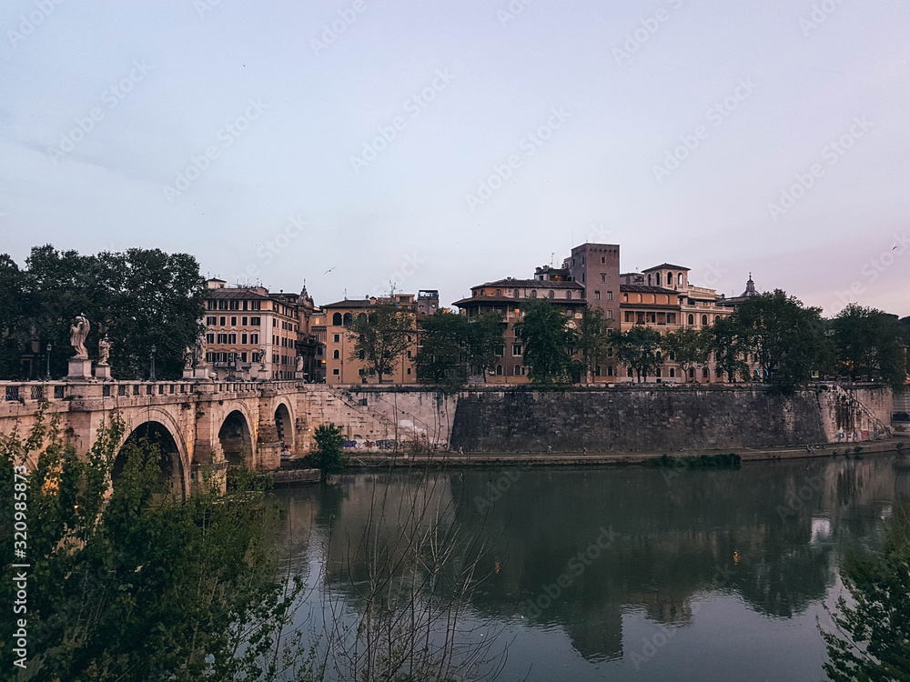 Beautiful river scene in Rome with a bridge and houses at early evening.	
