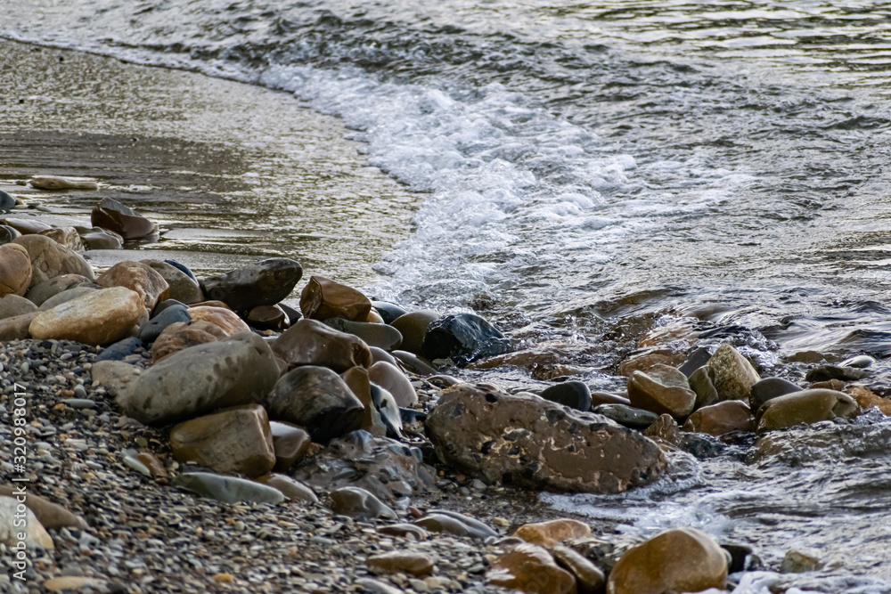 Obraz premium Large and smooth stones in the coastal waves of salty sea water. The coast of the black sea foams and roars, beating against a huge pebble, illuminated by sunlight