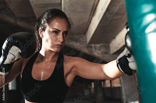 Female boxer punching a boxing bag in warehouse.