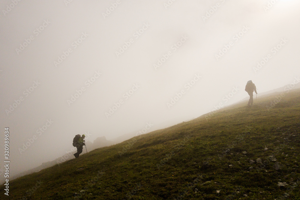 Group of tourists climb the mountain through the fog to the light.