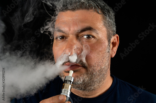 Mature man holding electronic vaping device, vaping with lots of smoke.