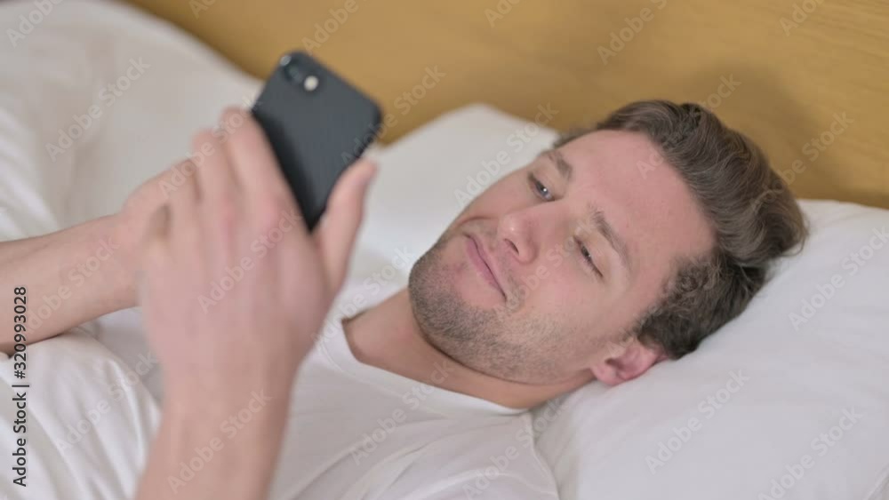 Portrait of Cheerful Young Man using Smartphone in Bed Portrait of Cheerful Young Man using Smartphone in Bed