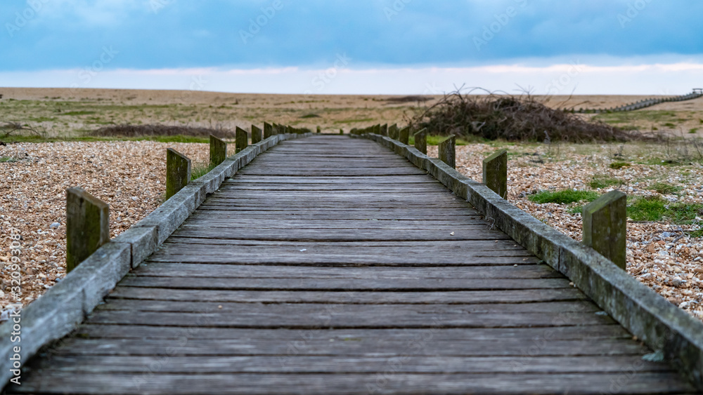 Wooden footpath heading out to shore over pebble beach. Central shot