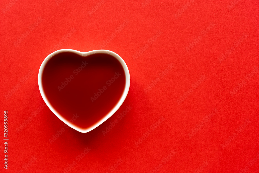 Valentine background. White porcelain heart filled with red liquid on a red background to be used as a template for valentine's day or wedding. Image with copy space.