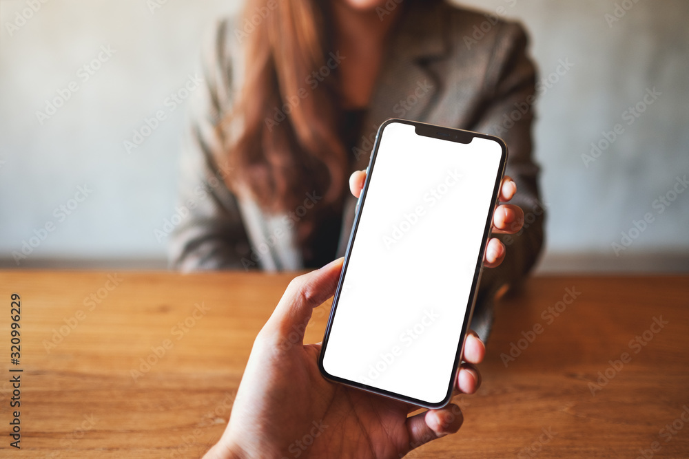 Mockup image of a woman holding and showing white mobile phone with blank black desktop screen to someone - obrazy, fototapety, plakaty 