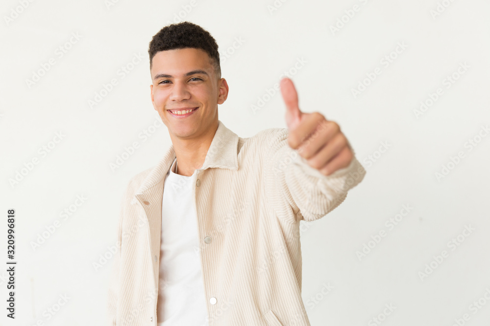 Handsome young man showing thumb up. Cheerful young man showing thumb up and smiling at camera isolated on white background. Approve concept Handsome young man showing thumb up. Cheerful young man showing thumb up and smiling at camera isolated on white background. Approve concept