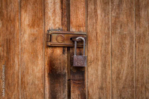 Vintage locked padlock with chain at brown wooden door background, Closeup © apimook