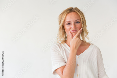 Unhappy woman with hand on chin. Portrait of blonde young woman with unpleasant facial expression standing with hand on chin and looking at camera. Emotion concept