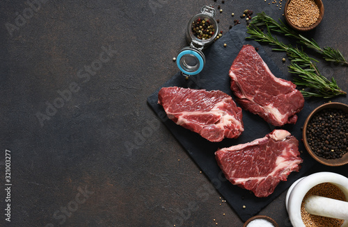 Raw marbled beef steak on a stone board. Spices, dishes. Top view flat lay with copy space.