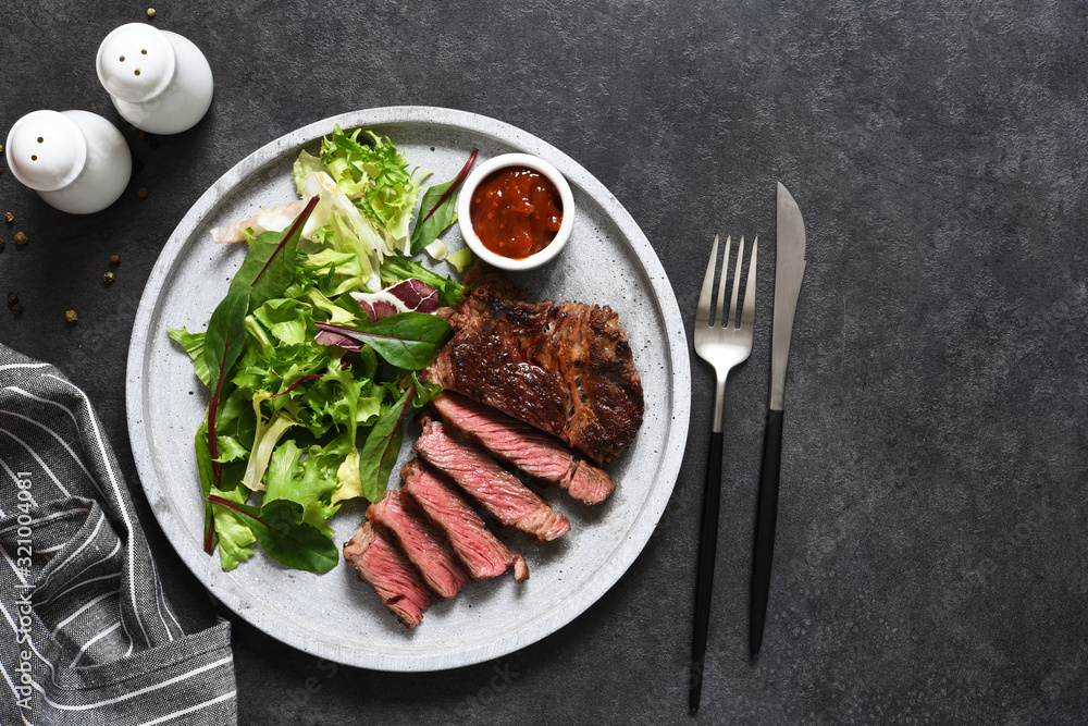 Grilled marbled beef steak with salad in a plate on the kitchen table. With copy space under the text. Grilled marbled beef steak with salad in a plate on the kitchen table. With copy space under the text.