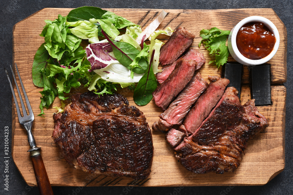 Grilled marbled beef steak with salad on a wooden board on the kitchen table. With copy space under the text.