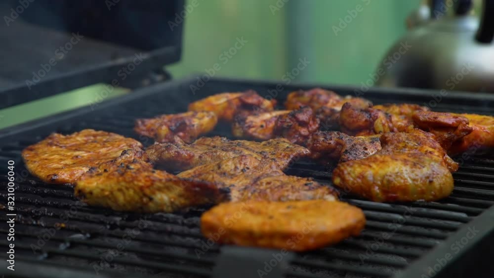 Closeup of Process of Grilling Delicious Chicken and Pork Meat on Barbecue Grill Outdoors. Slow Motion. Leisure, Food, People and Holidays Concept Closeup of Process of Grilling Delicious Chicken and Pork Meat on Barbecue Grill Outdoors. Slow Motion. Leisure, Food, People and Holidays Concept