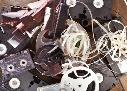 Vintage film camera rolls, old audio and video casettes with tape and foto strip on a wooden background.