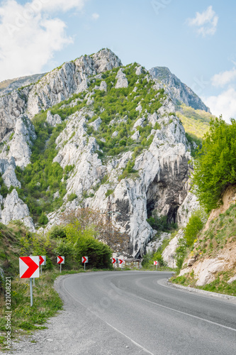 A dangerous turn on a mountain asphalt road, on the left a series of signs with reflective red arrows indicating the direction of the turn. High rocky hill in the background. Iskar Gorge, Bulgaria. photo