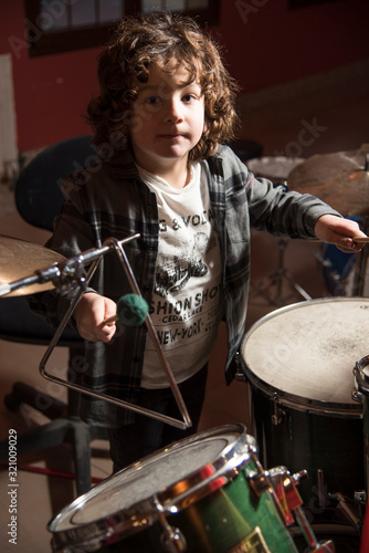 Curly-haired boy and gray shirt of shirtmakers playing drums like a pro. Fun and passion playing music