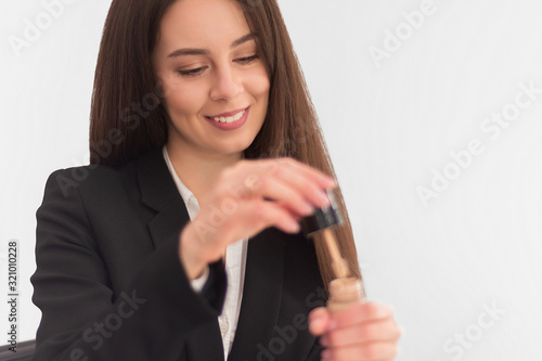 girl, makeup artist, with long dark hair in a business suit opens a tube with concealer on a white background