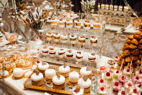 Table full with cakes and sweets at a wedding reception. Wedding candy bar and different cap cakes. Candy bar, a table with sweets and desserts on the table. Buffet with delicious cupcakes, flowers.