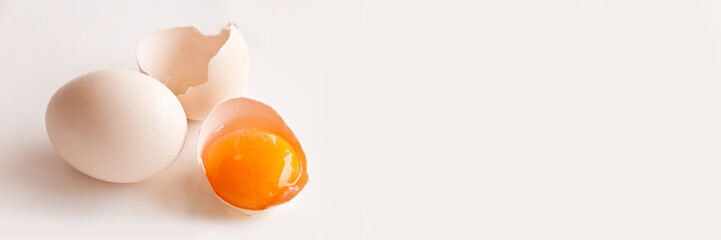 Broken egg and egg yolk on white panoramic background with copy space