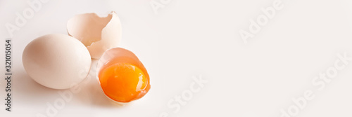Canvas Broken egg and egg yolk on white panoramic background with copy space