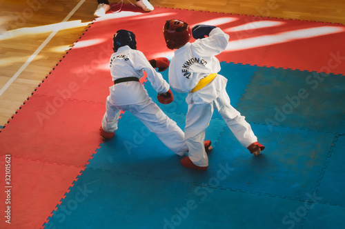 Martial Arts - Taekwondo. Kids in traditional kimano, hard hats and gloves. Sports duel. For atmospheric, a motion blur film noise effect has been added. Text: Taekwondo is the name for martial art.