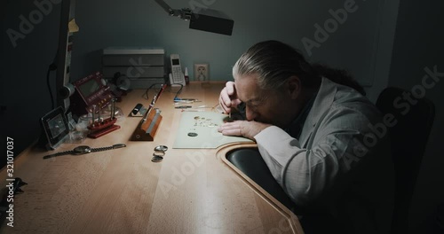 A watchmaker carefully removing the parts of a wristwatch he's repairing - wide shot photo