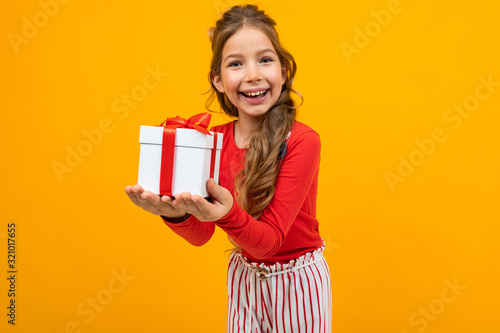 smiling caucasian girl in a red jumper with a gift box on a yellow background with copy space