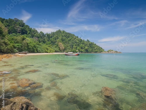 view seaside of a fishing boat floating in green sea with green island and blue sky background, Kwang Peeb Beach, Ao Kwang Peeb, Ko Phayam (ko payam), Ranong, Thailand.