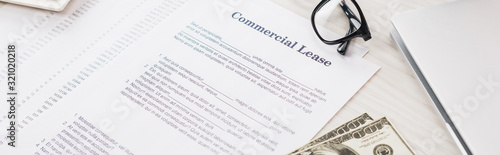 panoramic shot of documents with commercial lease lettering near money and glasses on desk
