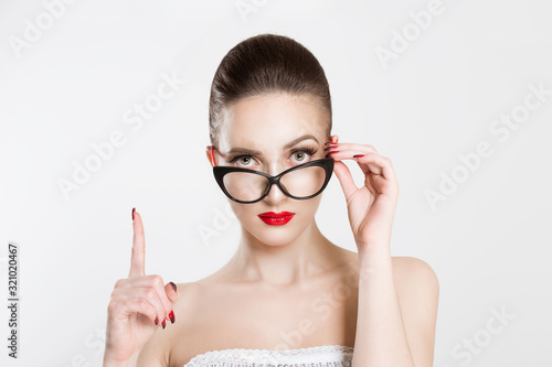 Attention listen to me. Close up portrait young woman wagging her finger holding glasses skeptically isolated white grey wall background. Negative human emotion face expression body language attitude photo