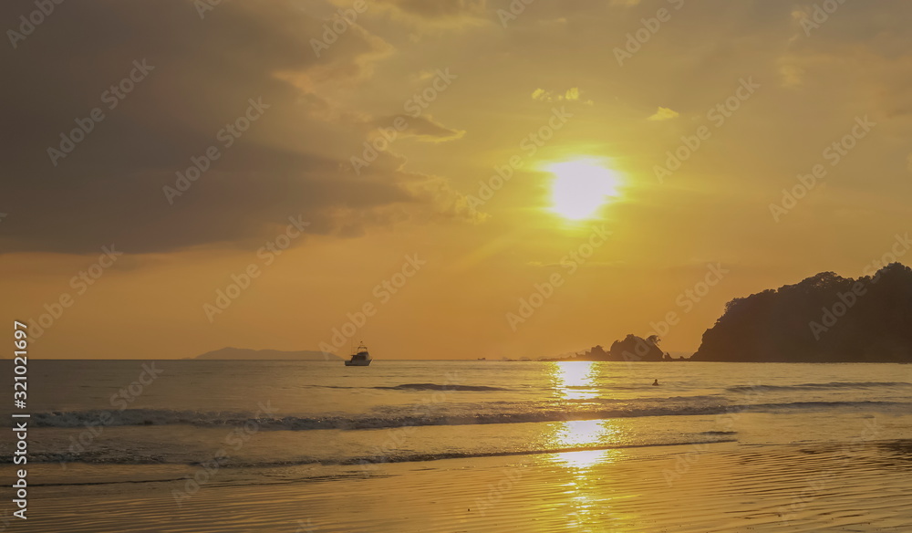 view seaside evening of mountain and small boat in the sea with yellow sun light in the sky background, sunset at Ao Yai Beach, Ko Phayam island, Ranong Province, southern of Thailand.