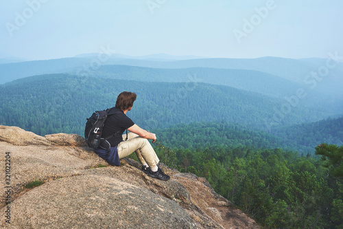 Male traveller with a backpack sitting at the rock at the Stolby Nature Reserve in Krasnoyarsk 