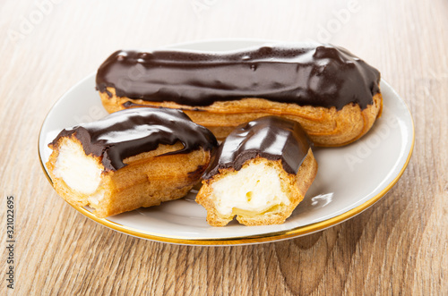 Fotografia Eclair with chocolate glaze, halves of eclair in saucer on wooden plate