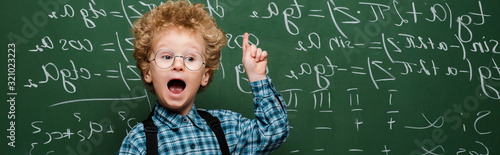 panoramic shot of kid in glasses having idea near chalkboard photo