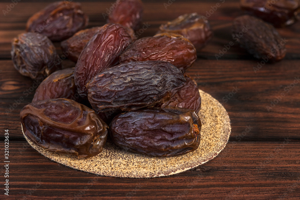 Tasty royal dates on a round substrate close-up on a wooden background Tasty royal dates on a round substrate close-up on a wooden background