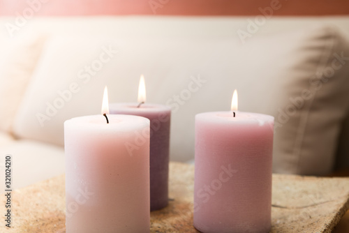 Group of three burning candles in the home. Candles of pink tones in a warm house. Sofa in the background