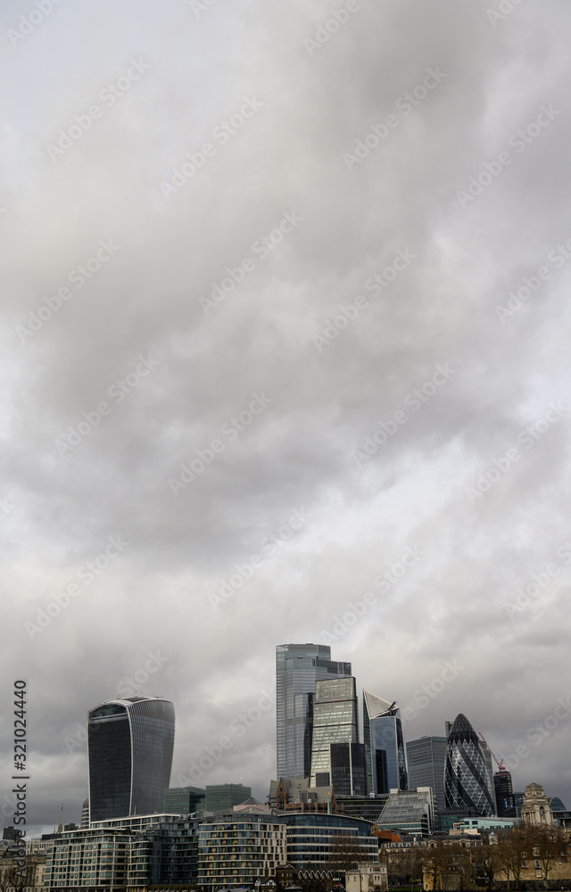 City of London in the UK. Portrait view over the River Thames to the city of London with dramatic grey stormy clouds. Cityscape of the business district of London with skyscrapers in 2020.