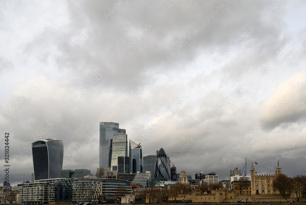 City of London in the UK. View over the River Thames to the city of London and the Tower of London with dramatic stormy clouds. Cityscape of the business district and Tower of London in 2020.