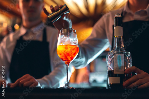 Barman hand stirring a fresh and sweet orange summer cocktail with a spoon on the bar counter. photo
