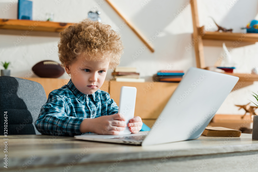 selective focus of smart child holding smartphone near laptop selective focus of smart child holding smartphone near laptop