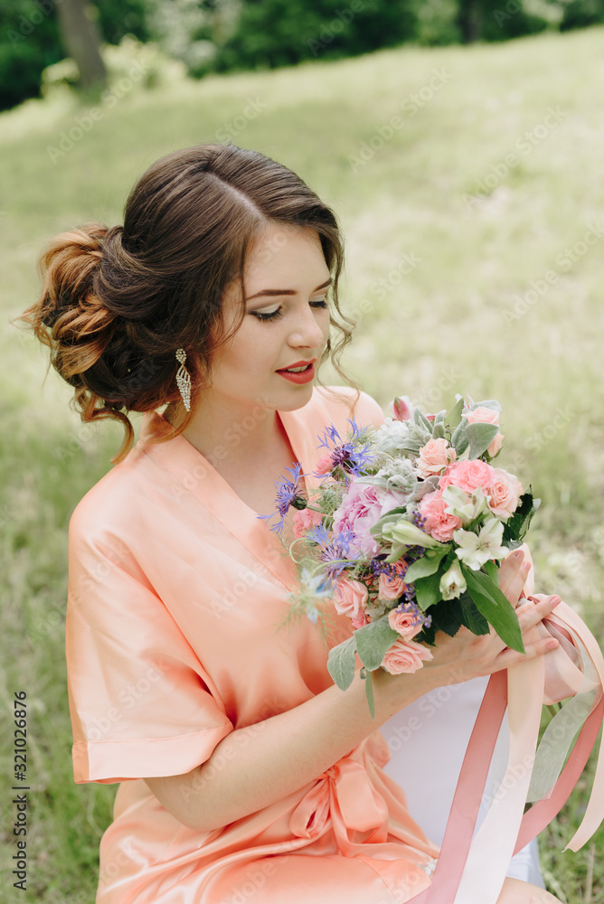 beautiful girl in a bathrobe with a bouquet of flowers on nature in summer on a background of green leaves
