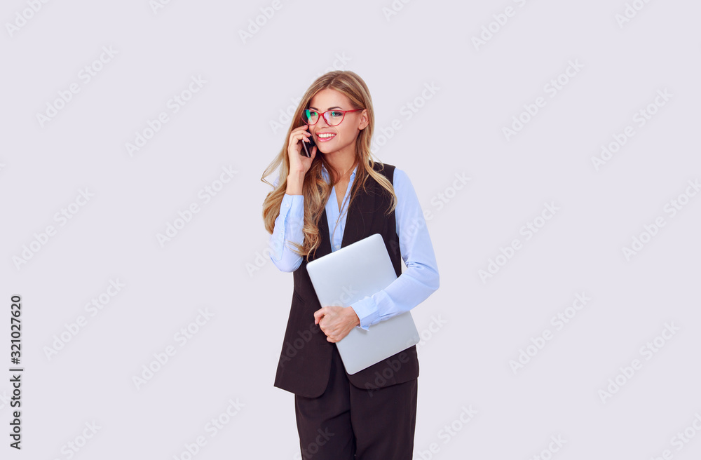 Phone talk. Happy woman smiling talking at mobile phone smiling with teeth, other hand holding laptop computer looking to the left side. Isolated light purple white wall background with copy space. Phone talk. Happy woman smiling talking at mobile phone smiling with teeth, other hand holding laptop computer looking to the left side. Isolated light purple white wall background with copy space.