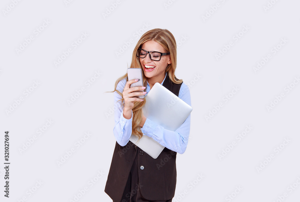 Good business news. Happy woman girl, female in eyeglasses using phone and holding laptop in other hand. Isolated light purple white background. Positive face expression Good business news. Happy woman girl, female in eyeglasses using phone and holding laptop in other hand. Isolated light purple white background. Positive face expression