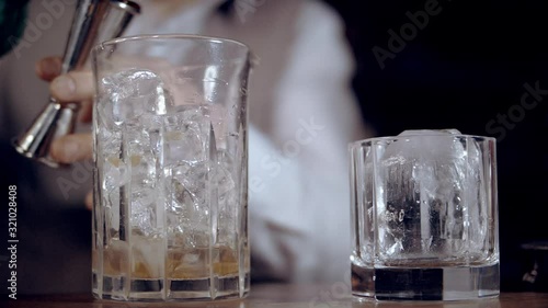 The bartender is preparing an Old Fashion cocktail. Bourbon is poured into a mixing glass with ice. Slow motion.