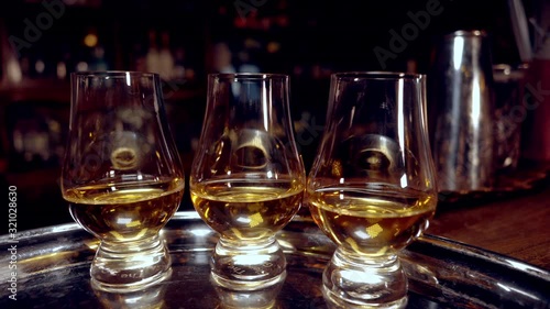 Three tasting glasses for whiskey  (glencairn) with a drink on a tray, with a fixed camera. Movement around the bar.