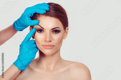 Upper eyelid blepharoplasty. Beautiful middle age woman getting ready for eyelid lift plastic surgery doctor hands in blue gloves point fingers to her eye on white. Beauty, people and health concept