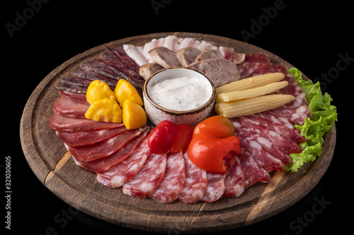 Delicious cold snack with different sausages and pickled vegetables on wooden board isolated on a black.