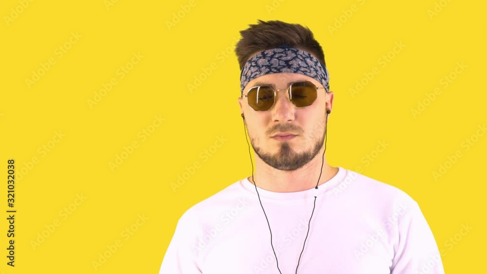 Stylish young man in white sweater and trendy glasses posing isolated over yellow background in studio. People sincere emotions lifestyle concept. Listen music in headphones Stylish young man in white sweater and trendy glasses posing isolated over yellow background in studio. People sincere emotions lifestyle concept. Listen music in headphones