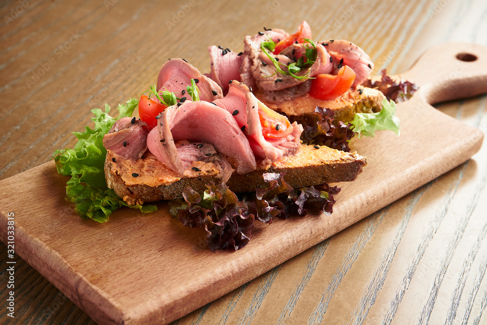 Traditional Italian antipasti - bruschetta with roast beef and tomato on a wooden board on a wooden background. Film effect during post. Soft focus Traditional Italian antipasti - bruschetta with roast beef and tomato on a wooden board on a wooden background. Film effect during post. Soft focus