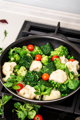  Cooking healthy organic food. Organic tomatoes, spinach, arugula, cauliflower and fresh green meat. Vegetarian food. Vegetables in a pan.